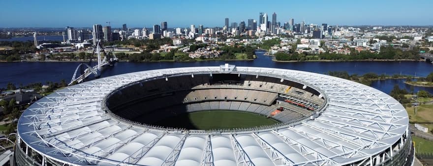 Optus Stadium in Perth seen from the air, with the city skyline behind it