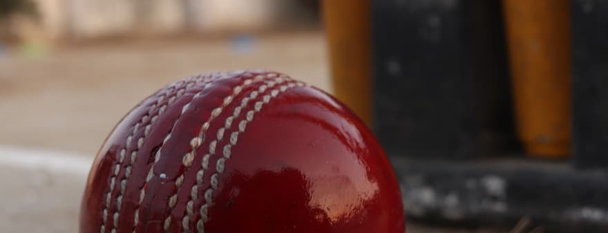 A red cricket ball on the ground in front of the stumps