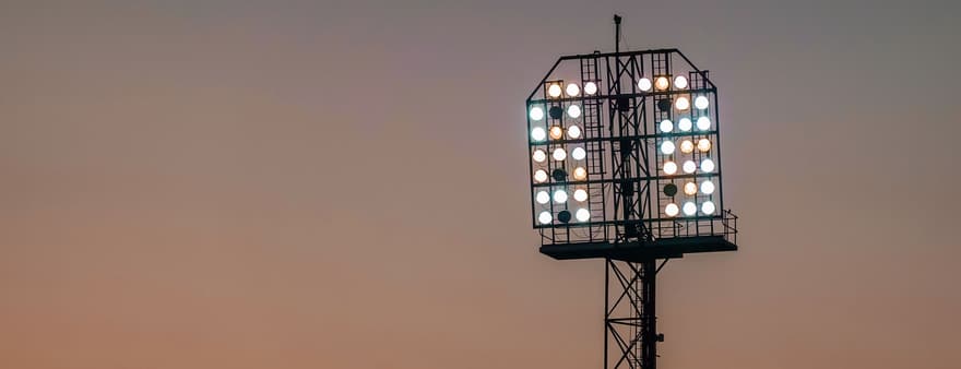 A stadium floodlight tower lit against a twilight sky