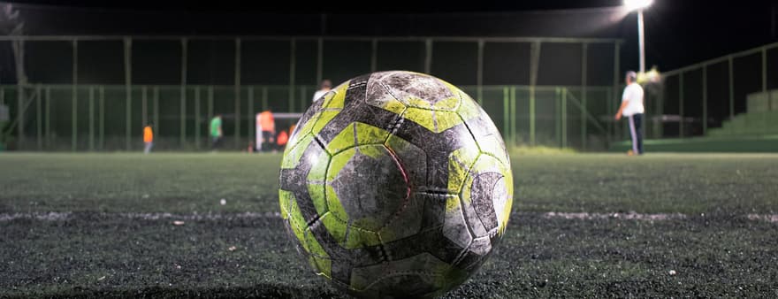 A football resting on a pitch at night under floodlights