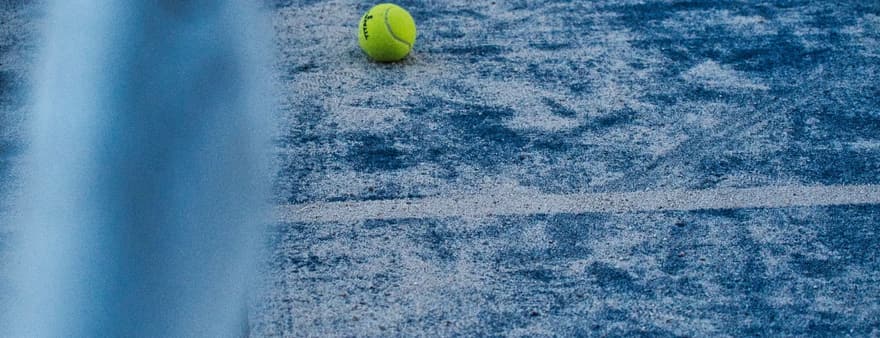 A tennis ball on a worn blue hard court